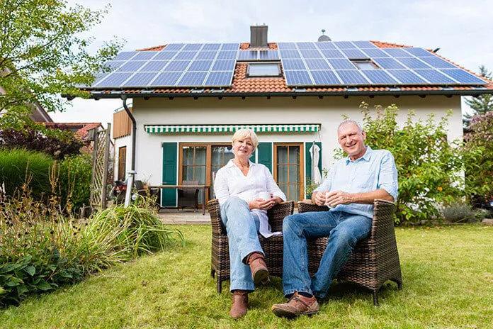 důchodci s domem a fotovoltaikou na pozadí